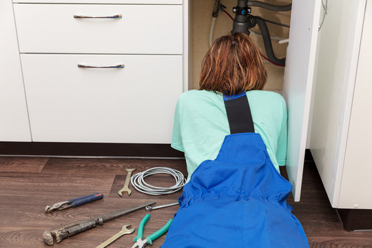 girl plumber puddle on her stomach looks under  sink in kitchen