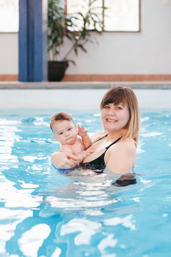 White Caucasian mother traning her newborn baby to float in swimming pool. Baby diving in water. Healthy active lifestyle. Family activity and early development concept