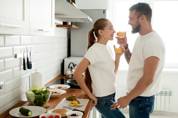 Young smiling couple preparing breakfast in cozy kitchen, loving man and woman drinking fresh...