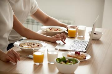 Couple having oatmeal and pancakes on breakfast using laptop on dining table, man and woman enjoying meal together and planning healthy eating or searching recipes online on computer, close up view