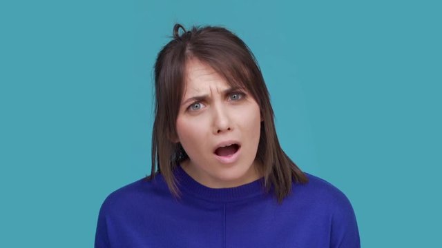 Portrait of upset woman expressing displeasure and aversion meaning are you kidding me or how it can be truth over blue background in studio. Concept of emotions