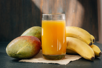 Glass filled by mango and banana juice over black surface.