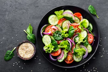 Foto op Plexiglas Gerechten Gezonde groentesalade van verse tomaat, komkommer, ui, spinazie, sla en sesam op plaat. Dieetmenu. Bovenaanzicht.