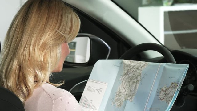 Close up of a gorgeous blonde mature woman smiling to the camera cheerfully after searching directions on a map sitting in a car travelling destination driving navigation transport auto.