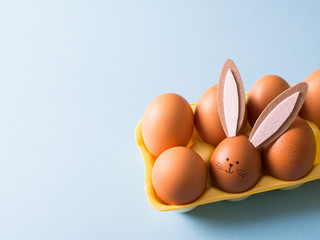 Eggs with easter bunny in yellow box on wooden background