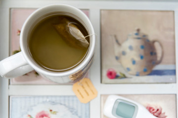 Cup of tea with tea bag on tray with digital thermometer