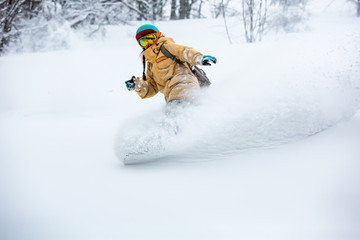 A snowboarder girl is riding down the hill. Powder day in mountains.