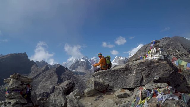 The guy sits on a rock high in the mountains. He looks at the map and plans a further path. Himalayas. Nepal. 4K