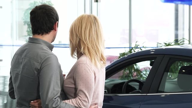Rearview shot of a husband and wife choosing a new car at the dealership salon looking at the automobiles to buy buying shopping consumerism family transport travel anniversary.