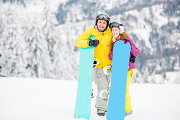 Fototapeta na wymiar Portrait of a young and happy couple standing with snowboards on the snowy mountains