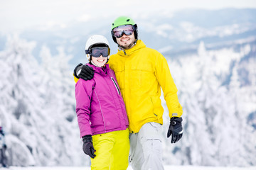 Fototapeta na wymiar Portrait of a young and happy couple snowboarders in colorful sports clothes standing together on the snowy mountains