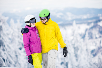 Fototapeta na wymiar Portrait of a young and happy couple snowboarders in colorful sports clothes standing together on the snowy mountains
