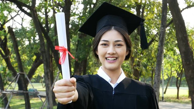 Young Asian Woman Students wearing Graduation hat and gown, Garden background, Woman with Graduation Concept. 
