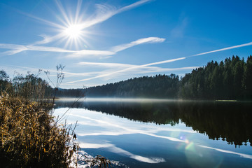 Sonnenstrahlen mit Nebel undüber dem See und Reflektionen im Wasser von Bäumen im Bayerischen Wald