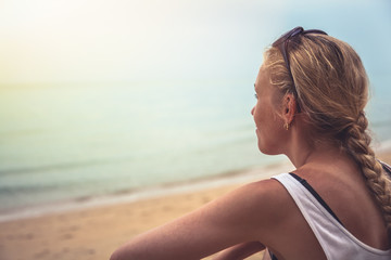 Pensive cheerful woman tourist relaxing on beach looking into horizon during sunset at tropical beach