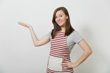 Young attractive smiling brunette caucasian housewife in striped apron isolated on white background. Beautiful housekeeper woman pointing hand aside looking camera. Copy space for advertisement.