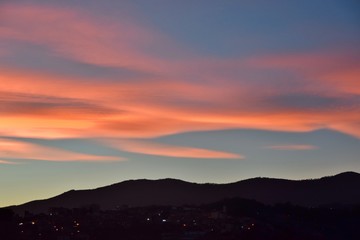 Obraz premium Zachód słońca z pomarańczowymi i różowymi chmurami na wzgórzu