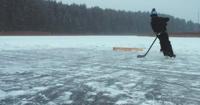 Kid playing pond hockey on a frozen lake alone. 4K UHD