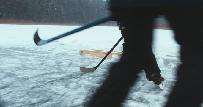 Father and son playing pond hockey on a frozen lake together, light snowfall. 4K UHD
