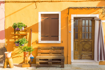 Obraz premium Yellow house with flowers and bench. Colorful houses in Burano island near Venice, Italy. Venice postcard. Famous place for european tourism and travel