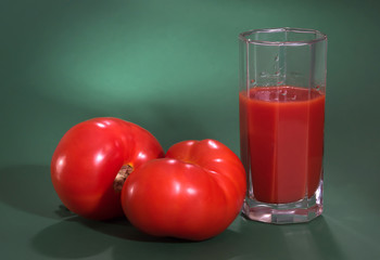 Red tomatoes and tomato juice on a green background,