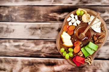Cheese plate - various types of cheese, honey, grapes, dried apricots, nuts and figs on a wooden board on dark wooden background.