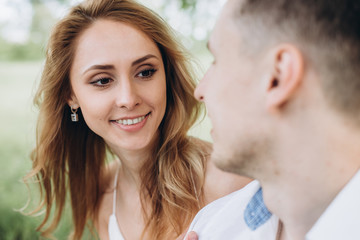 Fototapeta premium A beautiful blonde looks at her boyfriend with love and smiling. They are sitting on the grass.