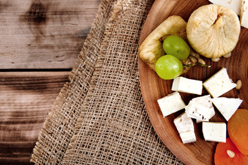 Cheese plate - various types of cheese, honey, grapes, dried apricots, nuts and figs on a wooden board on dark wooden background.