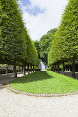 Green lawn between rows of trees leading to an open gate in an English landscaped garden, summer scene .