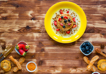 Homemade pancakes with fresh berries, strawberries, blueberries and maple syrup on a wooden background.