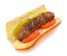 Grilled bratwurst, pickle and tomato on a bun isolated on white