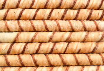 Heap of striped wafer tubules with the chocolate creamon background