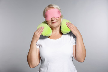 Senior woman with travel pillow and sleep mask on grey background