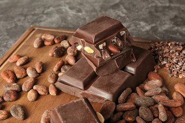 Wooden board with chocolate and cocoa products on table, closeup