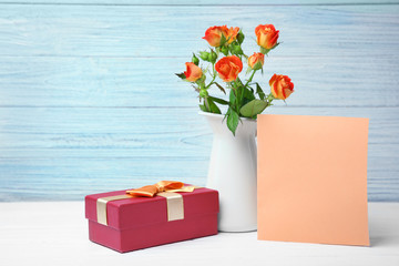 Roses, empty card and gift box on table