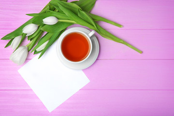 Tulips, card and cup of tea on pink wooden background