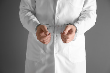 Male doctor in handcuffs on black background