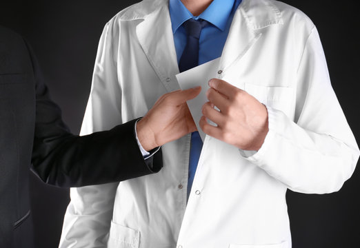 Businessman putting bribe in pocket of doctor's coat on black background