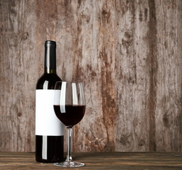 Glass of red wine and bottle with blank label on wooden table. Mock up for design