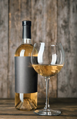 Glass of white wine and bottle with blank label on wooden table. Mock up for design