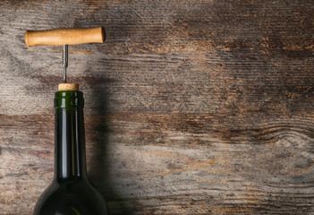 Bottle of wine with corkscrew on wooden background