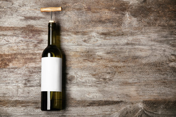 Bottle of wine with corkscrew and blank label on wooden background. Mock up for design