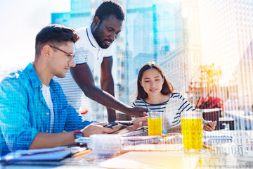 Discussing project. Handsome content afro-american man smiling and showing his part of work on the laptop to his co-workers and they discussing the project