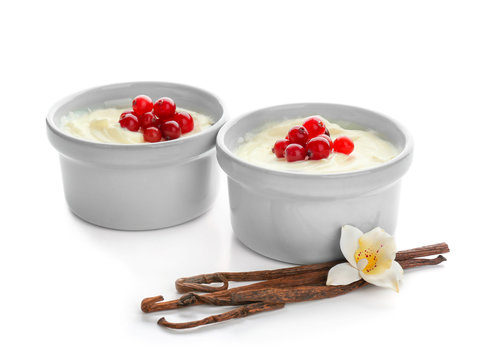 Tasty vanilla pudding with cranberry in ramekins and sticks on white background