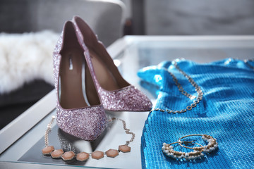 Beautiful high heeled shoes, dress and jewelry on table