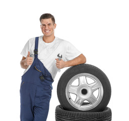 Young mechanic in uniform with car tires on white background