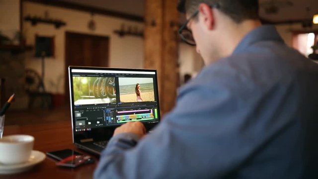 Freelancer video editor works at the laptop computer with movie editing sofware. Videographer vlogger or blogger camera man at work editing vlog. Tracking and revealing shot
