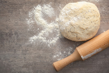 Raw dough with poppy seeds and rolling pin on table
