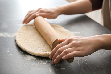 Obraz premium Hands rolling dough with wooden rolling pin on dark countertop, baking and cooking preparation process, fresh dough with poppy seeds is being flattened for a homemade meal