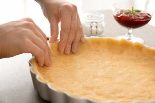 Woman making crust from dough in baking dish at table, closeup